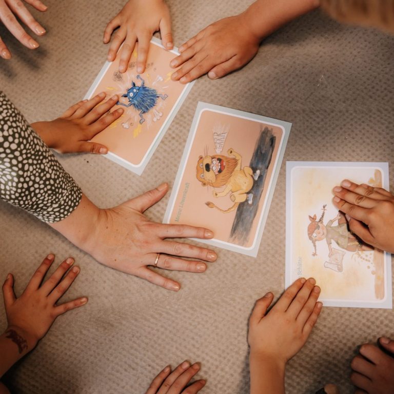 Mehrere Hände von Kindern liegen auf dem Boden und berühren drei Karten mit kindlichen Motiven.