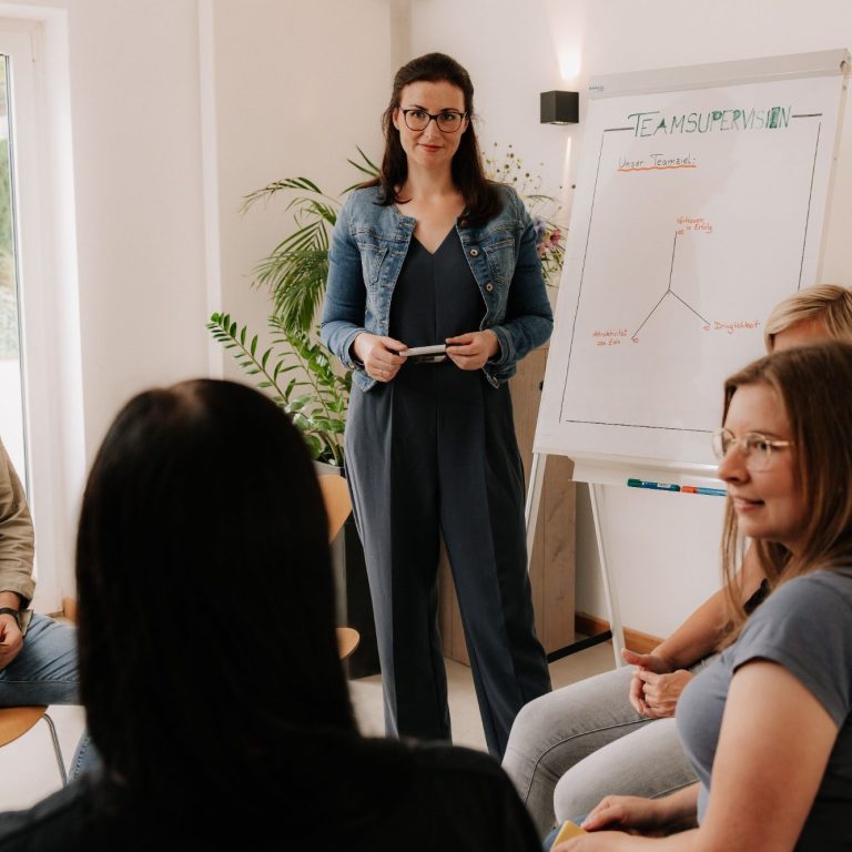 Evamaria Gerber steht am Flipchart und schaut zu einer sitzenden Supervisandin. 